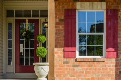 Close‑up of a window with red shutters, white trim, and horizontal siding.