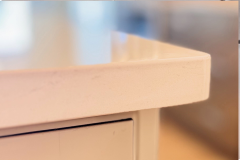 “Close‑up of light‑colored countertop corner with smooth surface and blurred background showing cabinetry below.