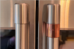 French-door stainless steel oven handles, one plain and one with a copper‑accent ring engraved with ‘CAFÉ.