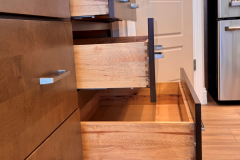 Close‑up of wooden kitchen drawers with modern rectangular metal handles, partially open to show wood grain and craftsmanship.