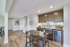 Bar area with wooden cabinetry, wine refrigerator, granite countertop with wine and glasses, wooden bar stools, and wood‑look flooring.