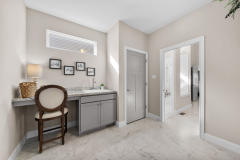 Laundry area with countertop, lamp, framed artwork, chair, light tile flooring, and two doors leading to adjacent spaces.