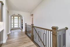 Hallway landing with wood flooring, white walls, railing with wood handrail and black balusters, and glass‑panel door with natural light.